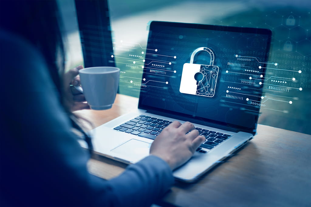 Person typing on a laptop with a digital padlock on screen, holding a cup of coffee